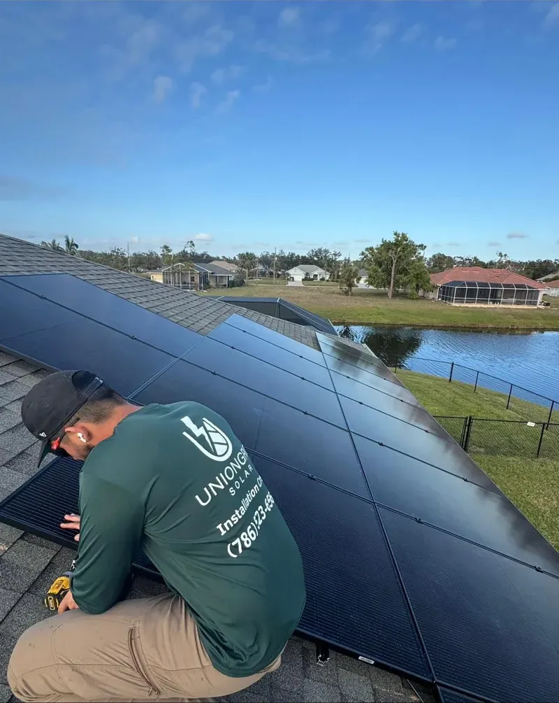UnionGrid installer kneeling on a shingle roof mounting solar panels beside a canal-front home in Cape Coral